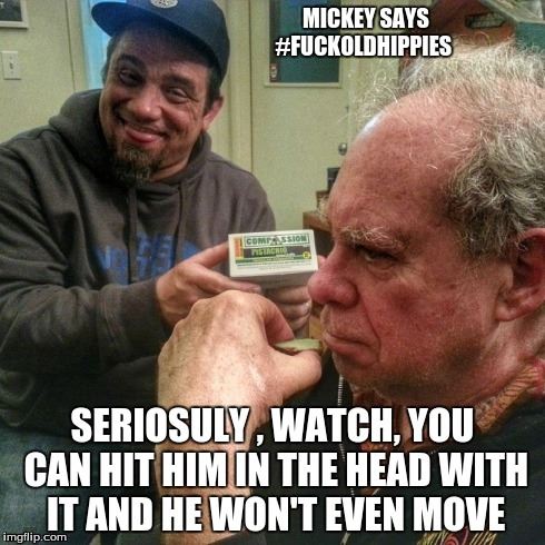 Mickey Martin smiling mischievously while holding a cannabis edible labeled "Compassion" near the head of Ed Rosenthal, a prominent cannabis expert, who sits calmly. Meme text overlay reads "MICKEY SAYS #FUCKOLDHIPPIES" and "SERIOUSLY, WATCH, YOU CAN HIT HIM IN THE HEAD WITH IT AND HE WON'T EVEN MOVE."