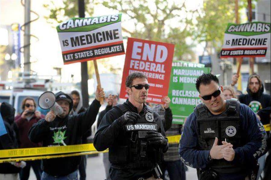 Protesters gather during a 2008 DEA raid on a medical marijuana shop in Oakland. They hold signs that support cannabis legalization and states' rights. U.S. Marshals stand in the foreground.